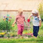Buntes Relaxdays Windrad aus Eisen mit Erdspieß im Garten, spielende Kinder. Dekorative Gartenfigur.