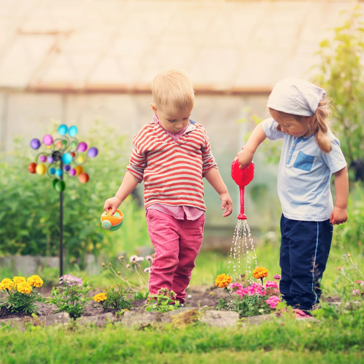 Buntes Relaxdays Windrad aus Eisen mit Erdspieß im Garten, spielende Kinder. Dekorative Gartenfigur.