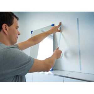 Mann befestigt Spiegel mit LUX Montageband an Wand. Doppelseitiges Klebeband für sicheren Halt.