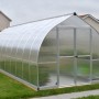 Silbernes Palram Canopia Bella Gewächshaus (6x2.4m) mit Stegplatten im Garten.