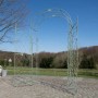 Antik-grüner Metall-Rosenbogen mit Tor als Rankhilfe und Gartendekoration auf gepflastertem Weg im Garten.