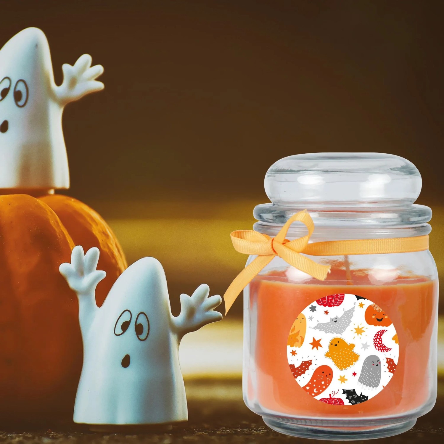 Orangefarbene HS Candle Duftkerze im Glas mit Halloween-Motiv und Geister-Deko.
