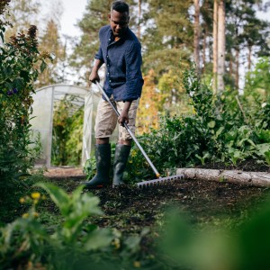 Mann harkt Erde mit Fiskars Ergonomic Rechen im Garten.