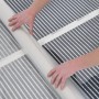 Aufgerollte Heizfolie zur Fußbodentemperierung mit grauen Heizleitern und weißen Streifen.