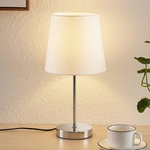 Moderne Lindby Tischlampe Leza aus Chrom-Metall mit weißem Schirm auf Holztisch. Ideal für Wohnzimmer.