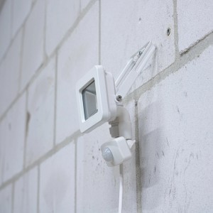 Weißer LED-Außenstrahler mit Sensor (10W, 1100lm, 4000K) an einer Wand montiert.