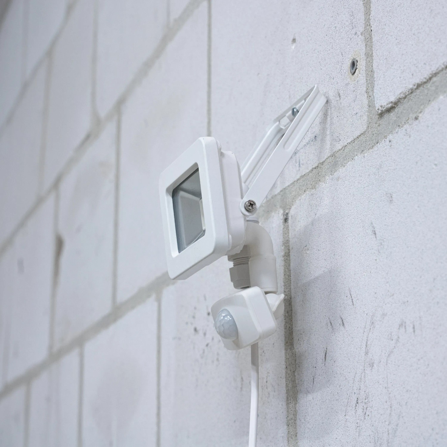 Weißer LED-Außenstrahler mit Sensor (10W, 1100lm, 4000K) an einer Wand montiert.