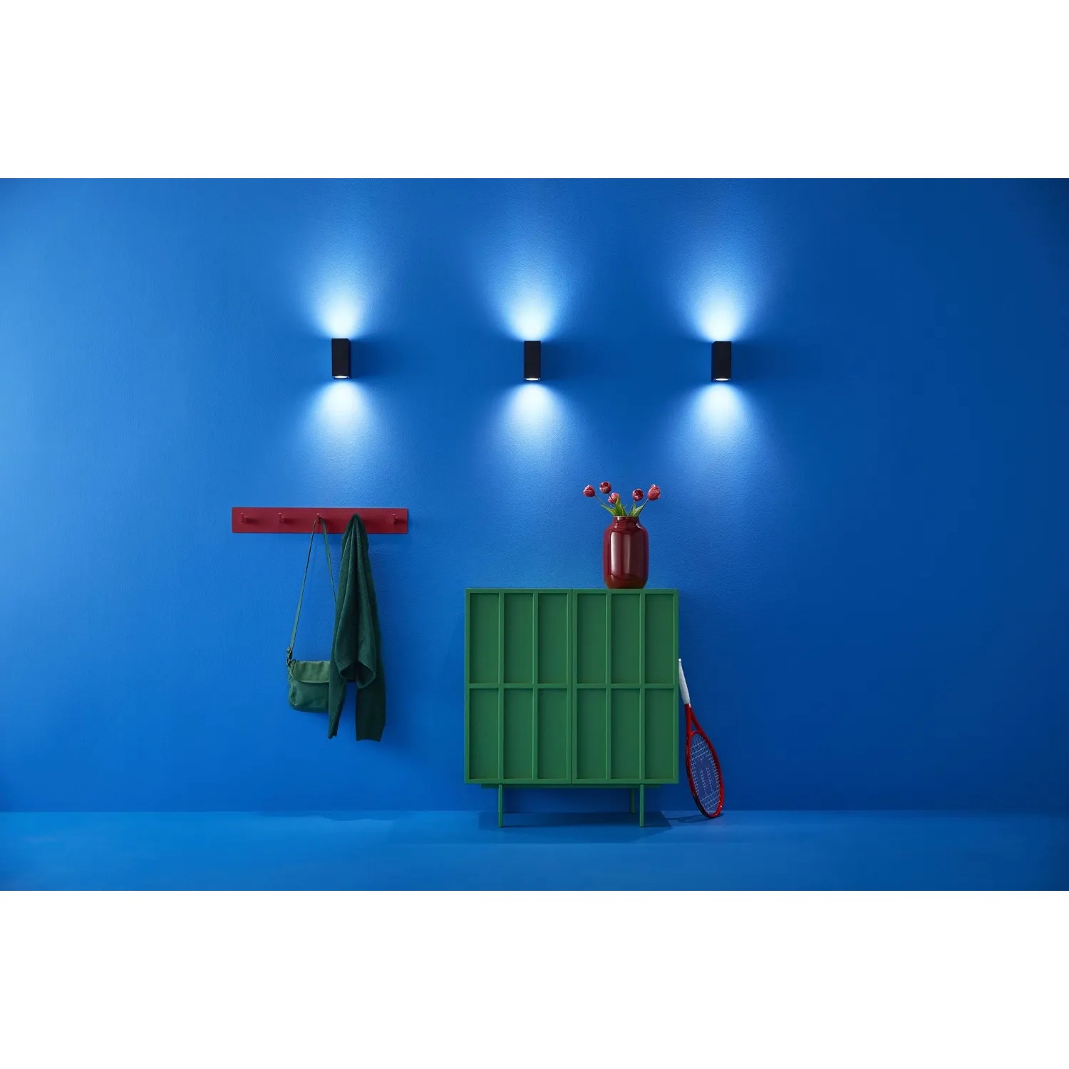 Drei schwarze WiZ LED Wandleuchten Up&Down an blauer Wand. Smarte Leuchten mit tunable White & Color, 690 lm.