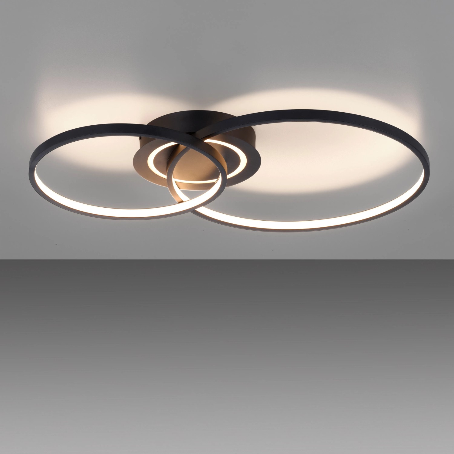 Moderne LED-Deckenleuchte Asmina in Schwarz mit verschlungenen Ringen, warmweißes Licht.