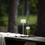 Zwei weiße Konstsmide LED Tischleuchten Lille auf einem Holztisch im Außenbereich.