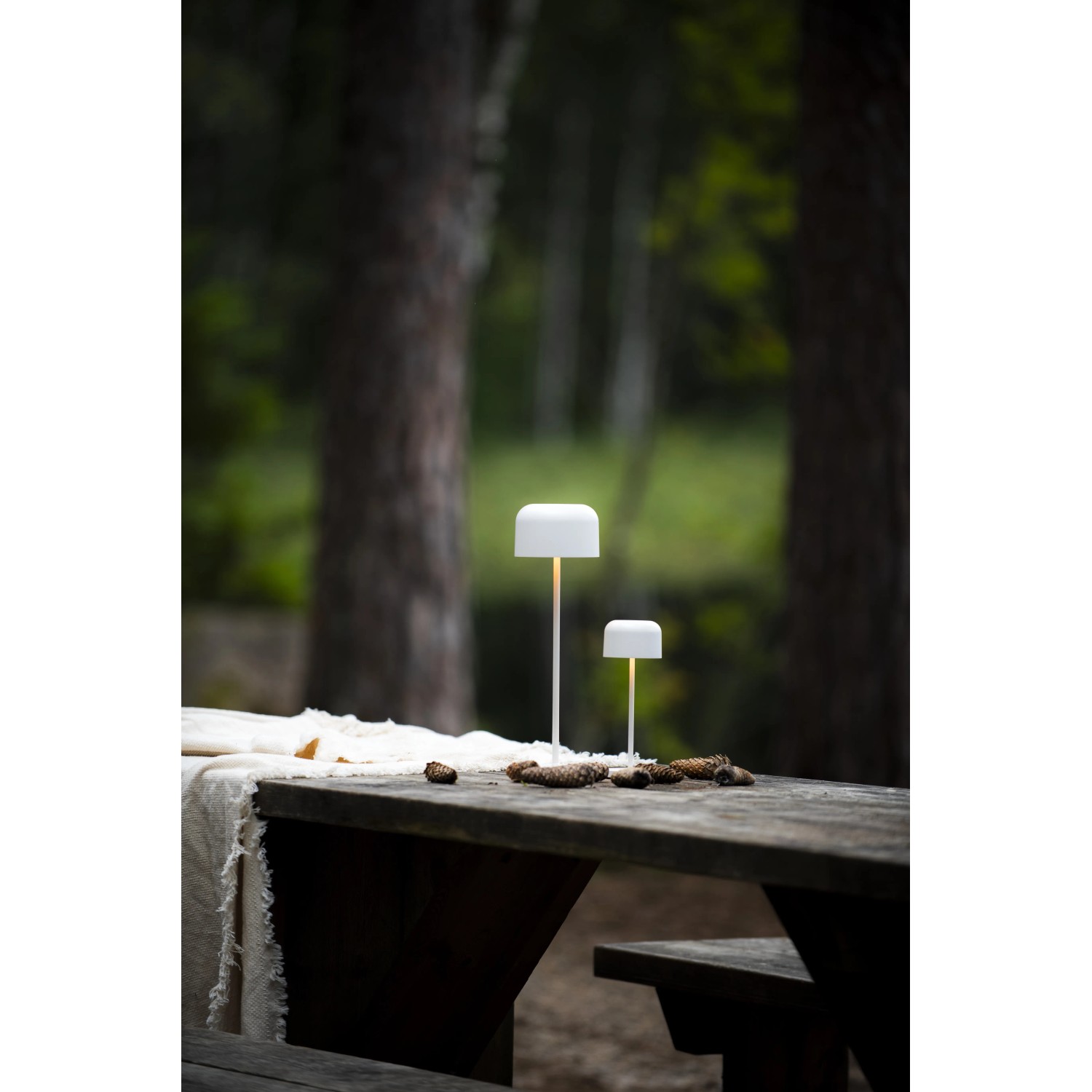 Zwei weiße Konstsmide LED Tischleuchten Lille auf einem Holztisch im Außenbereich.