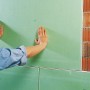 Anbringen einer grünen Gipskartonplatte mit Knauf Perlfix Ansetzgips an einer Ziegelwand.