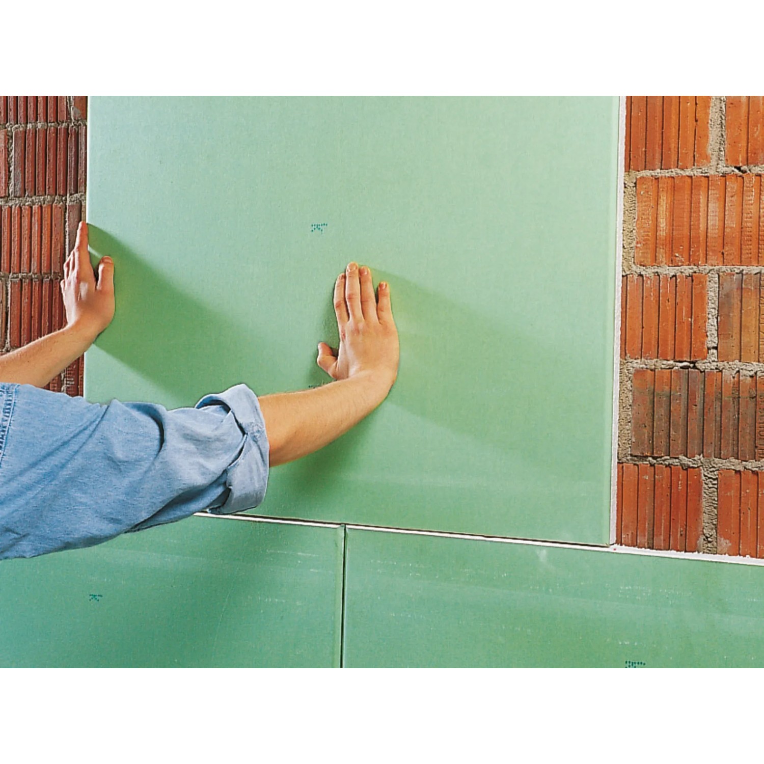 Anbringen einer grünen Gipskartonplatte mit Knauf Perlfix Ansetzgips an einer Ziegelwand.