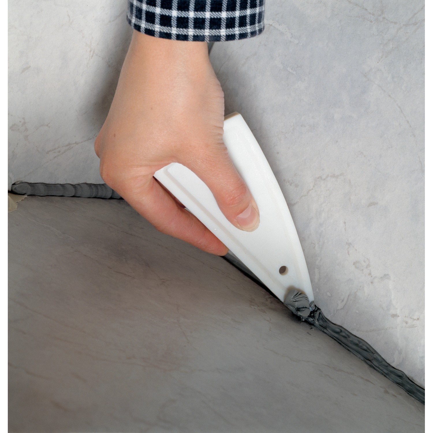 LUX Fugenglätter in Anwendung: Hand glättet graue Silikonfuge an Fliese. Maurerwerkzeug für saubere Fugen.