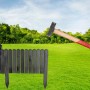 Grauer Holz Rollzaun als flexible Beeteinfassung auf grünem Rasen, teilweise ausgerollt, mit Hammer zur Montage.