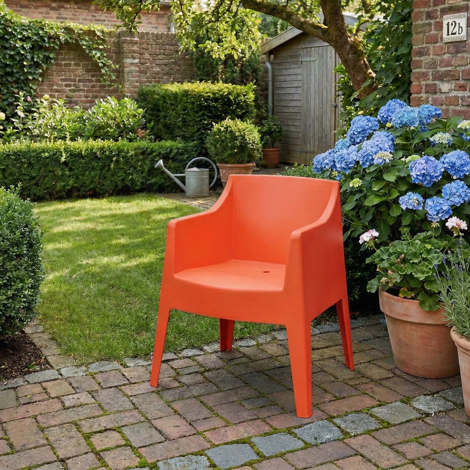 Oranger Kunststoff Gartenstuhl HENRI mit Armlehnen auf gepflasterter Terrasse im Garten. Stapelbarer Loungestuhl.