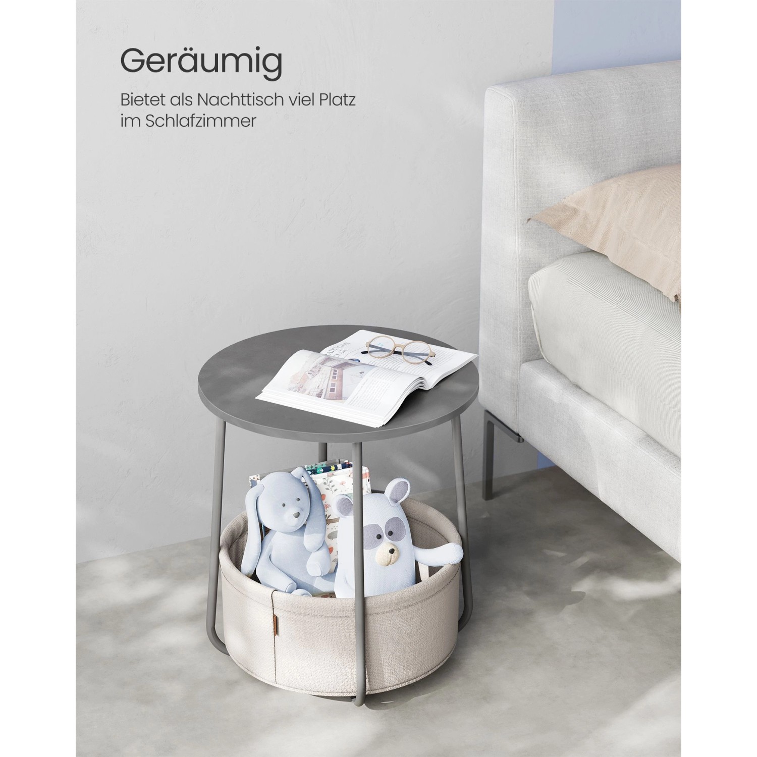 Grau-weißer Vasagle Beistelltisch (Ø 45 cm) mit Stauraumkorb neben einem Bett.
