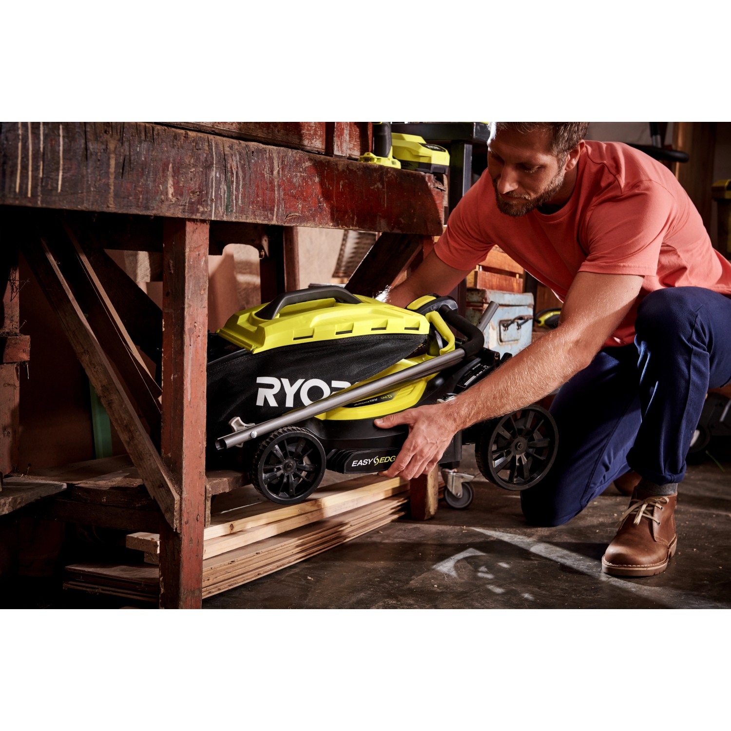 Zusammengeklappter Ryobi Akku-Rasenmäher RLM18X33B40 mit Fangsack und gelben Akzenten wird verstaut.