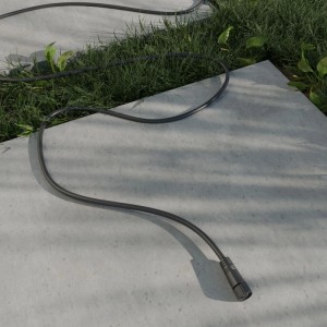 Schwarzes 1m Verlängerungskabel für 24V Garten-Lichtsysteme auf Pflastersteinen mit Gras.