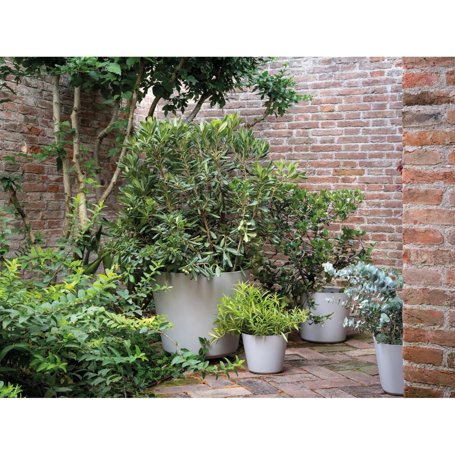 Helle, graue Deroma Pflanztöpfe (Origin Plant Pot) in verschiedenen Größen im Garten.