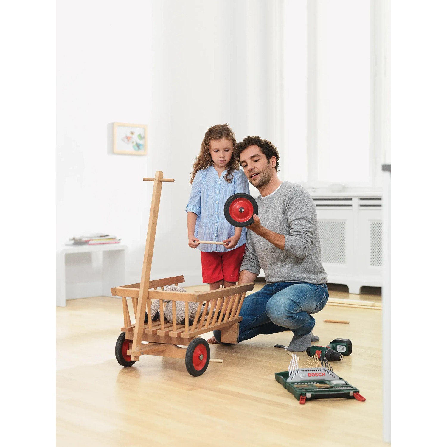 Mann und Kind bauen Holzwagen mit Bosch X-Line 70-teilig Zubehörbox und Zangen-Set.