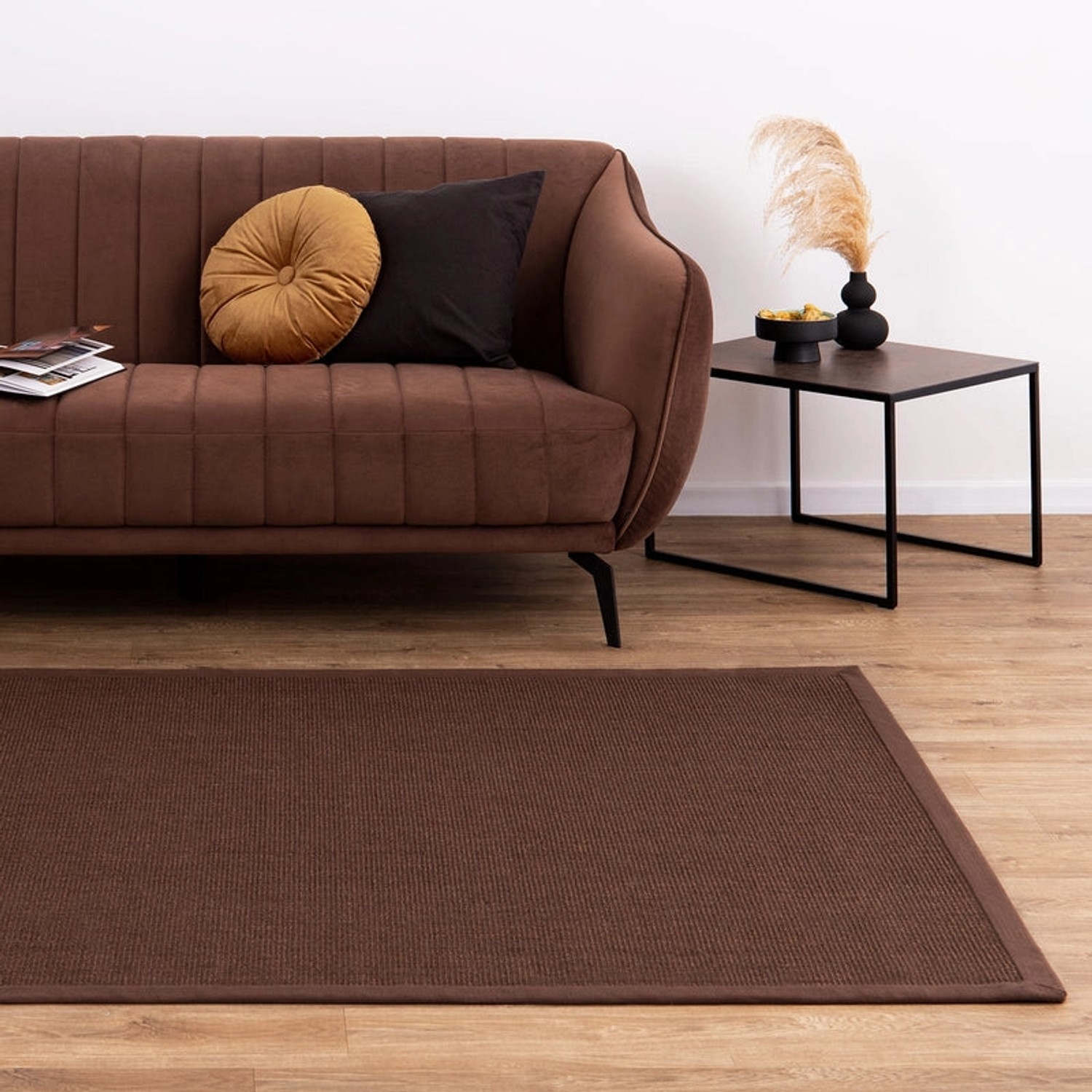 Dunkelbrauner KARAT Sisalteppich Amazonas mit breiter Bordüre im Wohnzimmer.