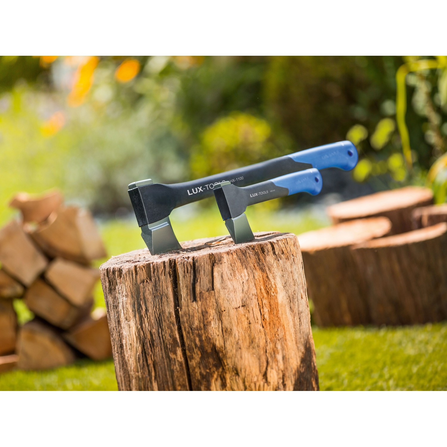 Zwei LUX Universalaxt Professional auf Holzblock, Garten im Hintergrund.