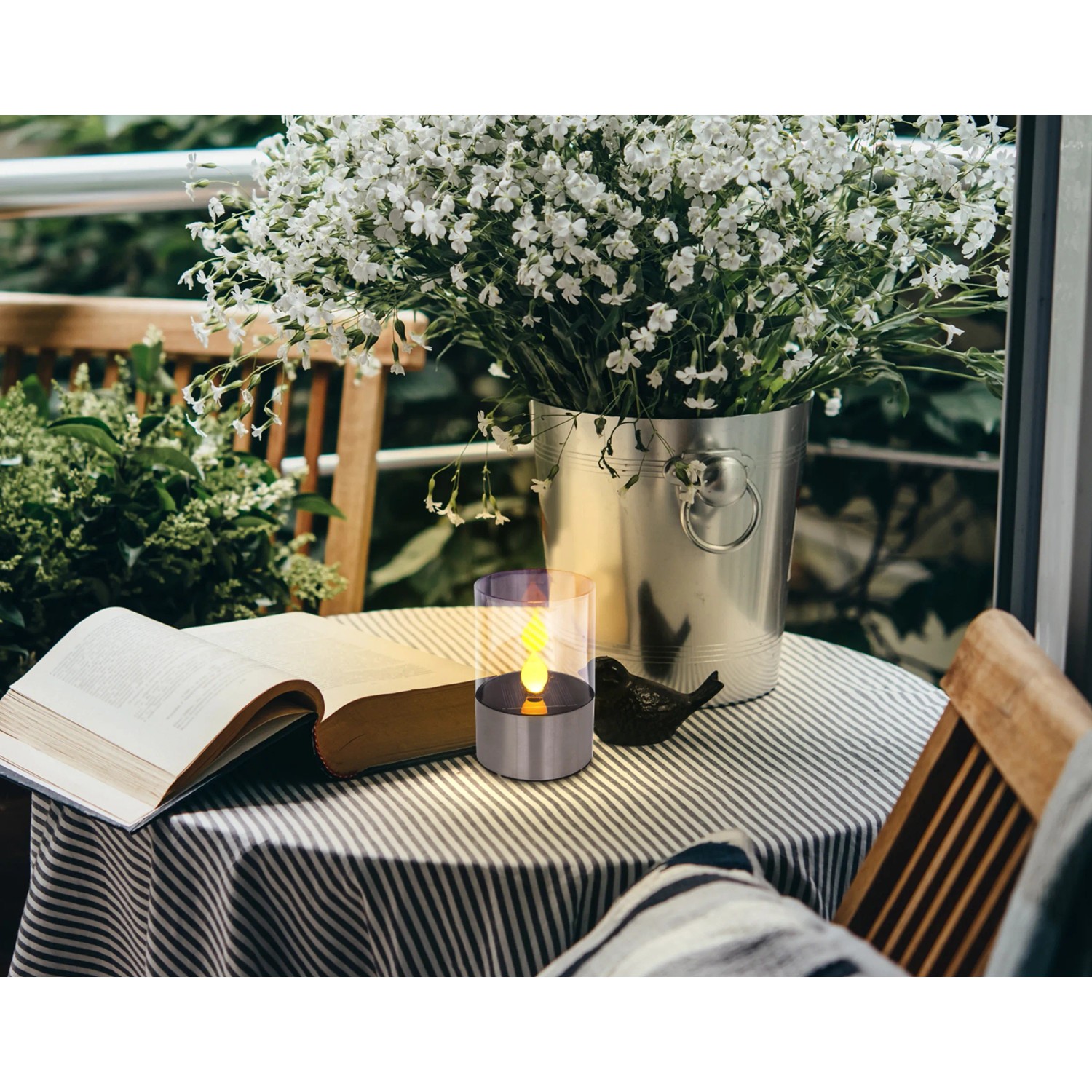 Globo LED-Solartischlampe mit Feuereffekt aus Edelstahl auf Tisch mit Buch und Blumenvase.