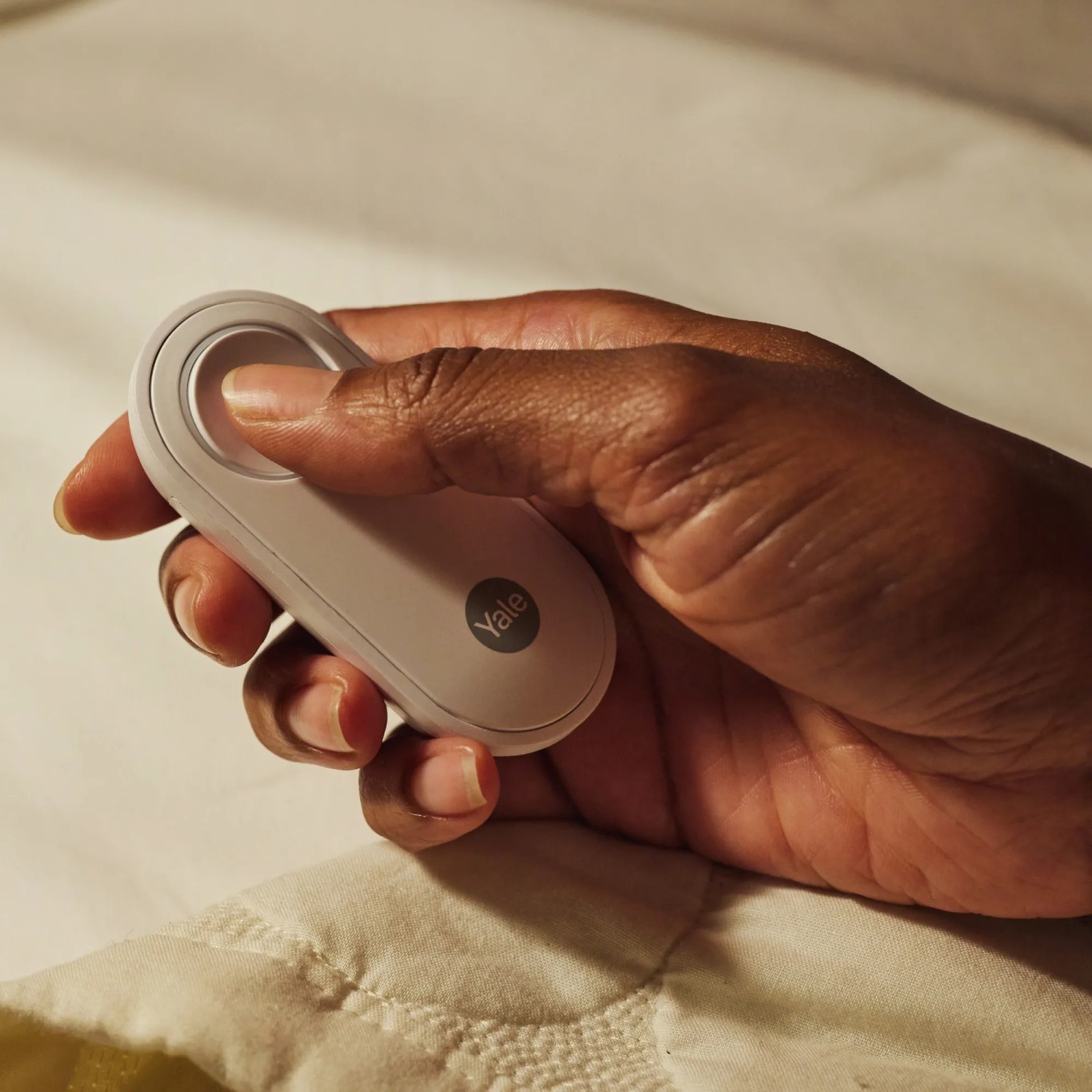Hand hält weißen Yale Panikknopf/Türklingel für Smart Alarmanlage.