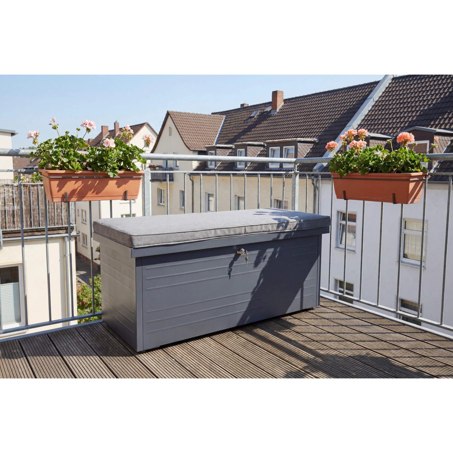 Anthrazitfarbene Stahl Aufbewahrungsbox mit grauem Sitzkissen auf Holzbalkon. Ideal als Gartenbox oder Bank.