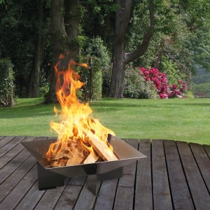Quadratische Wilk Feuerschale Karo 56x56x25 cm mit brennendem Holz im Garten.