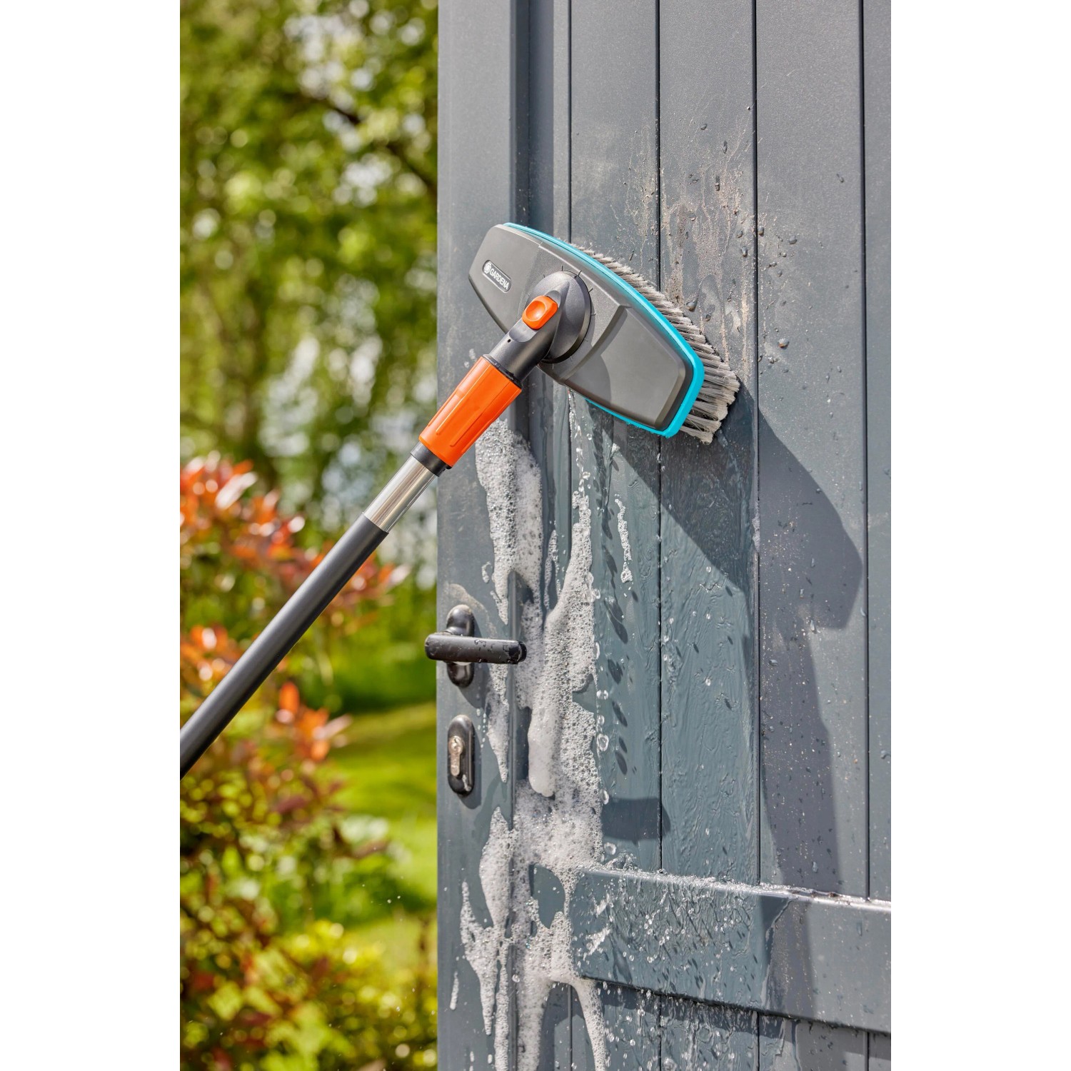 Gardena Cleansystem Stielbürste Soft in Aktion beim Reinigen einer grauen Tür mit Schaum.