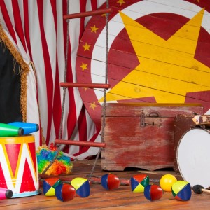 Bunte Jonglierbälle in Rot, Blau, Gelb, Grün auf Holzboden, umgeben von Zirkusrequisiten. Für Spiel & Spaß.