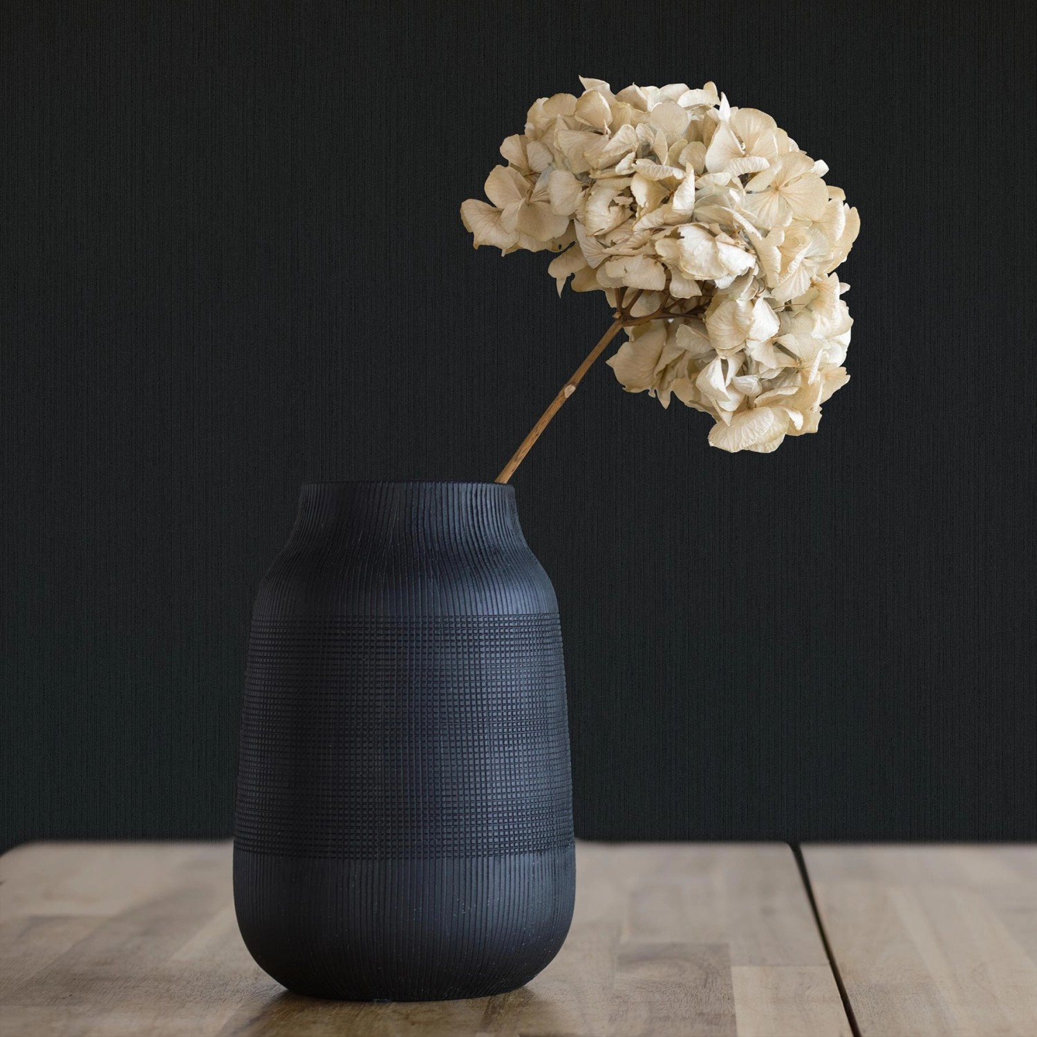 Schwarze Tadessi Vliestapete Uni mit Vase und Trockenblume im Raum.