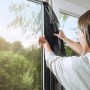 Frau montiert anthrazitfarbenes Tesa Pollenschutzgitter am Fenster.