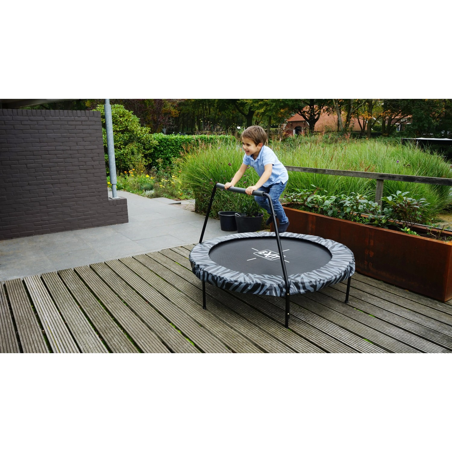 Kind springt auf EXIT Tiggy Junior Trampolin (Ø140cm) in Schwarz-Grau mit Haltebügel im Garten.