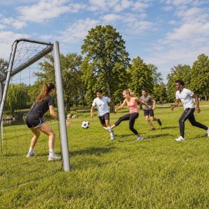 Graues Stahl-Fußballtor mit Netz im Garten, junge Erwachsene spielen Fußball. Perfekt für Sport & Training.