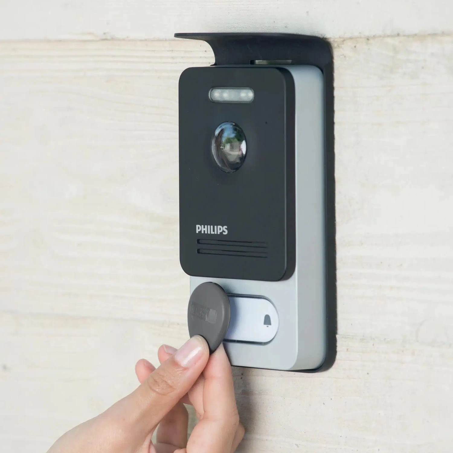 Philips WelcomeEye Connect 2 Video-Türsprechanlage, dunkelgrau/silber, an Wand. Hand nutzt RFID-Tag für Zutritt.