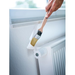 Hand streicht mit LUX Eckenpinsel (35mm) Heizkörper weiß. Pinsel mit Holzgriff und Kunstborsten.