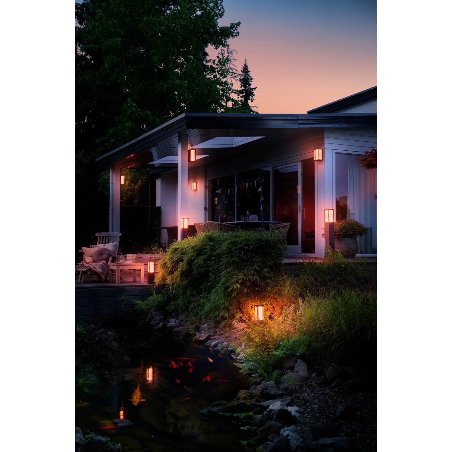 Philips Hue Impress LED-Wandleuchten in breiter Anordnung an Hauswand und Garten.