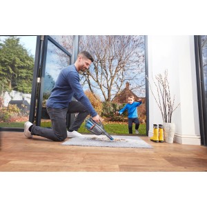 Mann saugt mit Black+Decker Akku-Handstaubsauger Teppich, Kind im Hintergrund.