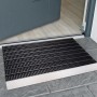 Schwarze Alu-Fußmatte (43x75 cm) vor einer grauen Haustür auf grauen Fliesen.