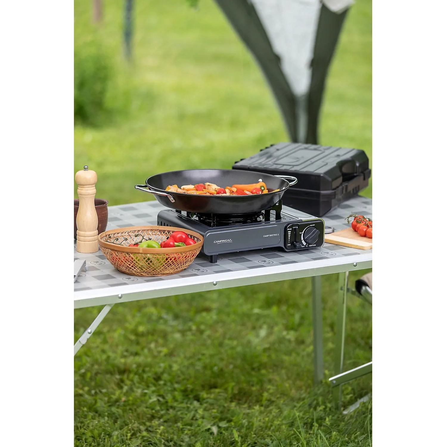 Campingaz Camp'Bistro 3 Tischkocher mit Pfanne und Gemüse auf einem Campingtisch im Grünen.