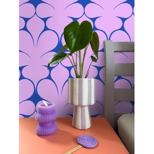 ESTAhome Tapete: Lila Wand mit blauen Retro-Ornamenten. Eine Pflanze in gestreifter Vase und lila Kerze auf orangefarbenem Tisch.