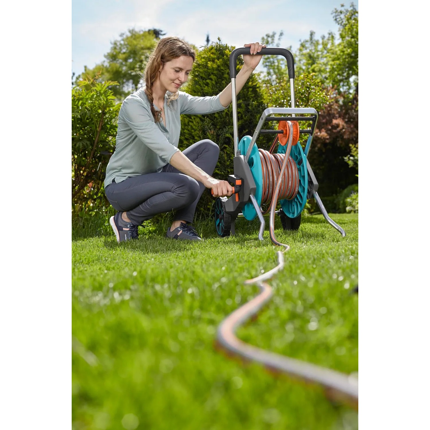 Frau bedient Gardena CleverRoll M Schlauchwagen-Set mit 20m Schlauch im Garten.