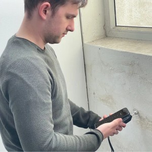 Mann misst Schimmel mit dem PCE Instruments Schimmel Messgerät an einer Wand.