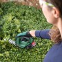 Frau schneidet Hecke mit Bosch Akku Gras- und Strauchschere AdvancedShear 18V-10. Kabellose Grasschere im Einsatz.