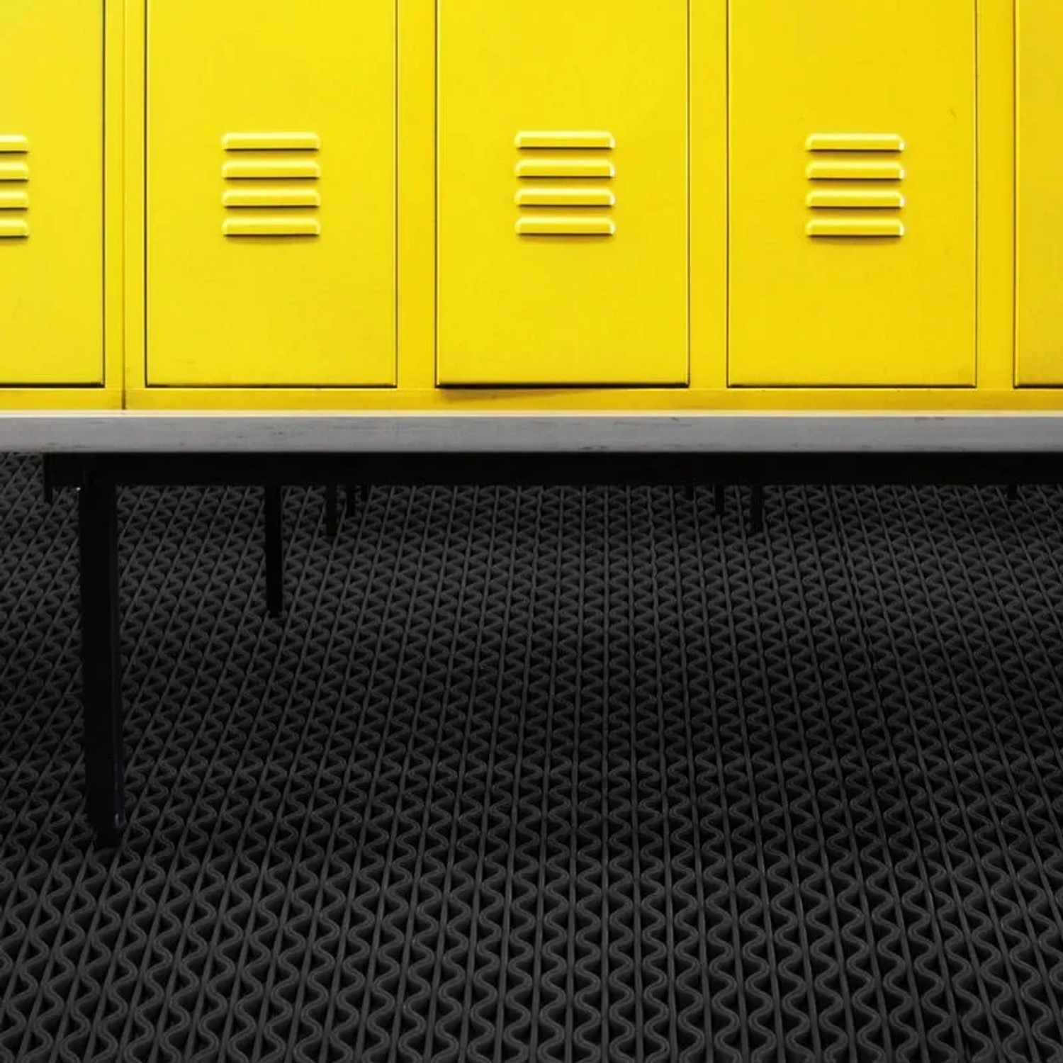 Schwarze KARAT Hygienematte 120x1100cm für Barfußzonen vor gelben Spinden.