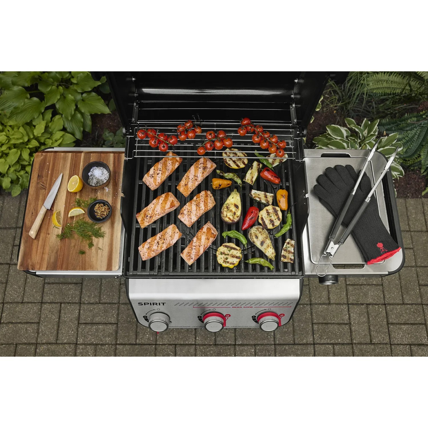 Weber Gasgrill E-310 Spirit mit Grillgut und Zubehör auf Seitentischen.