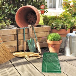 Grüner Relaxdays Folientunnel für Gewächshäuser, zusammengefaltet auf Holzterrasse mit Gartengeräten.